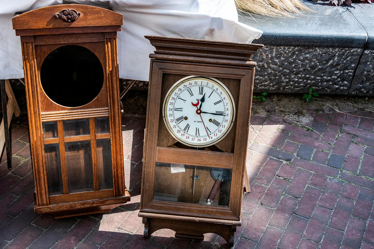Two old wall clocks in a brown wooden case outside on the street