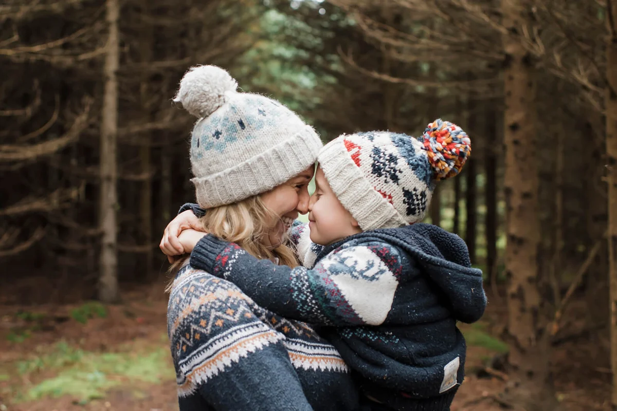 happy mother carrying cute son while standing against trees in forest