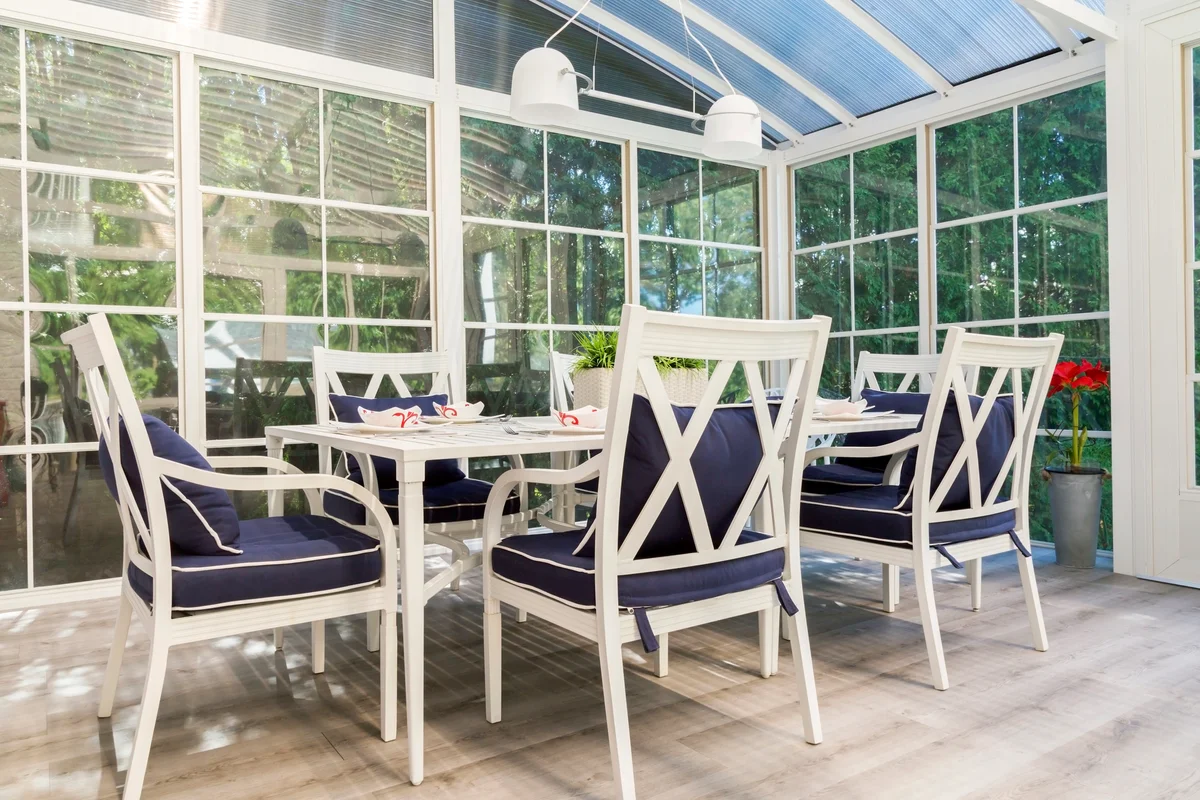 White dining table and armchairs with blue cushions in sunroom