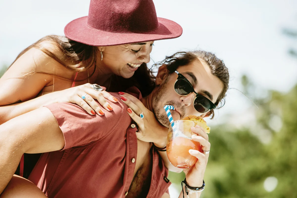 Young woman piggybacked by man sipping cocktail