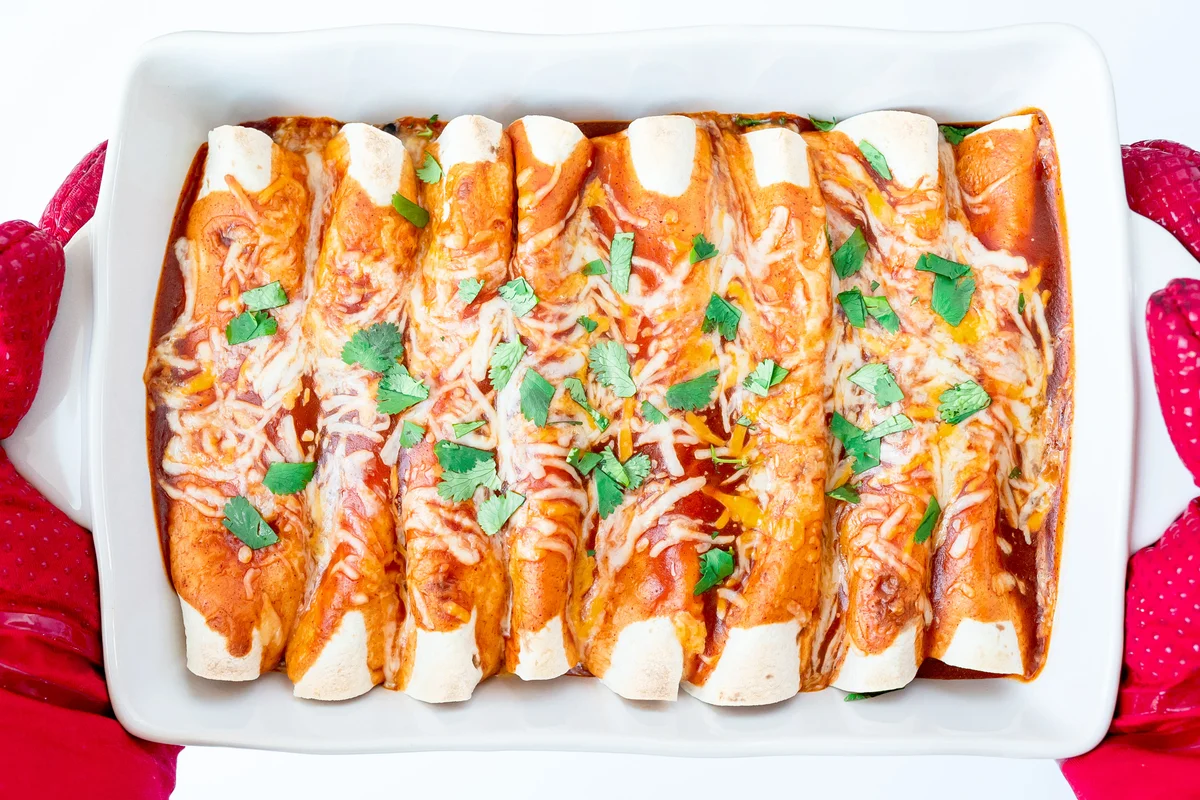 Mitts Holding White Baking Dish Filled with Beef Enchiladas