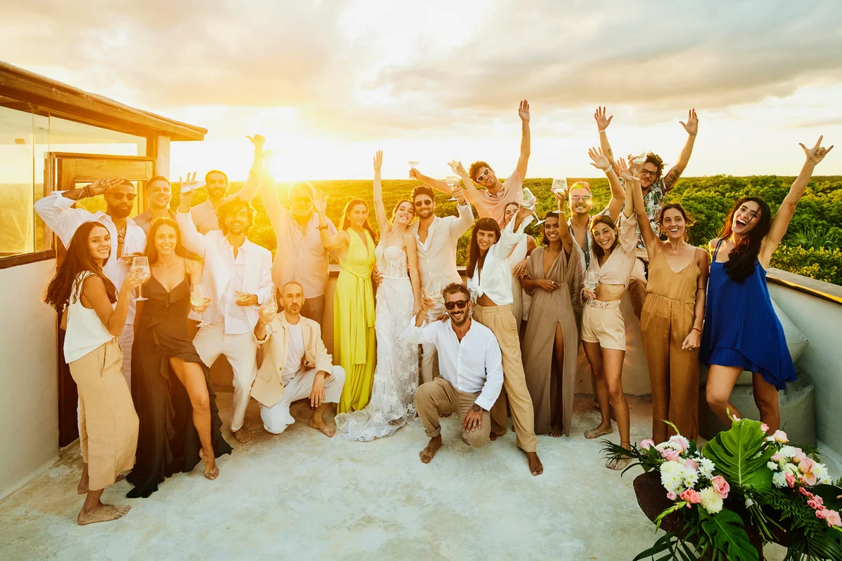 Wide shot of bride and groom embracing while family and friends celebrate after wedding ceremony on tropical beach