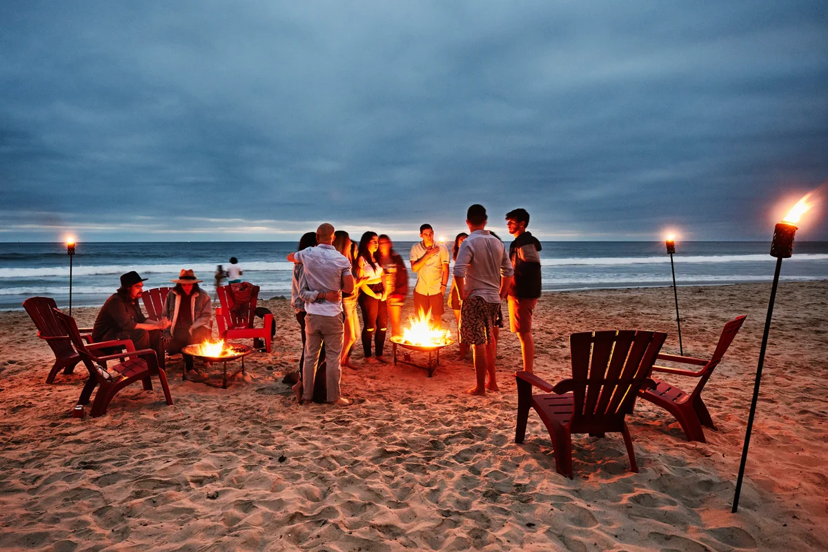 Friends gathered around fire on beach on summer evening