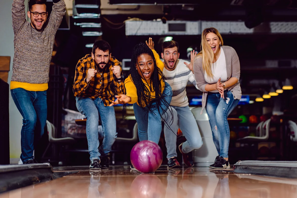 Group of friends enjoying time together laughing and cheering while bowling at club