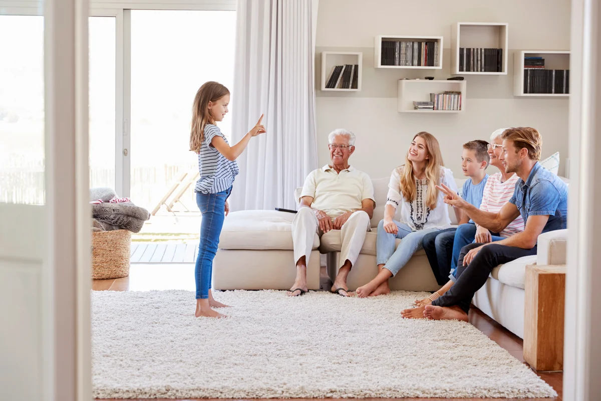 Multi Generation Family Sitting On Sofa At Home Playing Charades