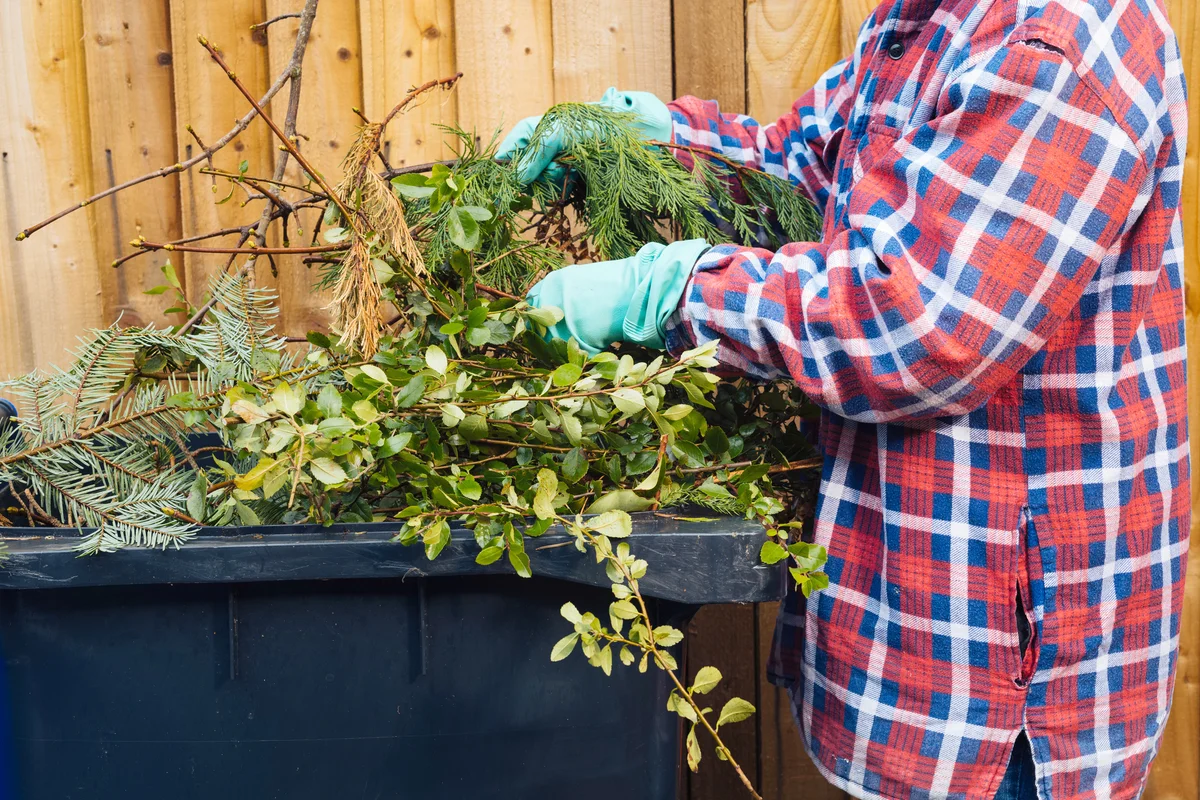 Woman putting garden clippings into a large plastic garbage bin