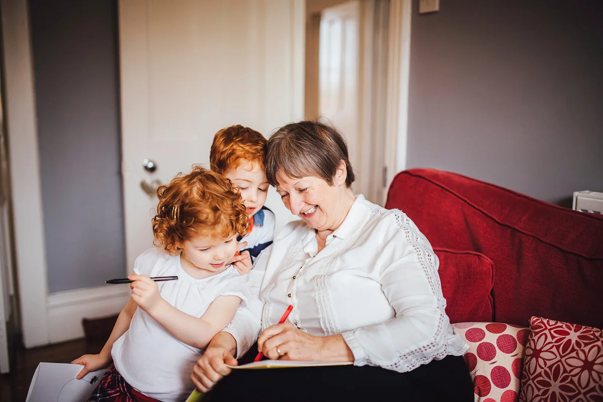 Little redheaded girl sits beside her brother and grandmother as she writes and draws for them