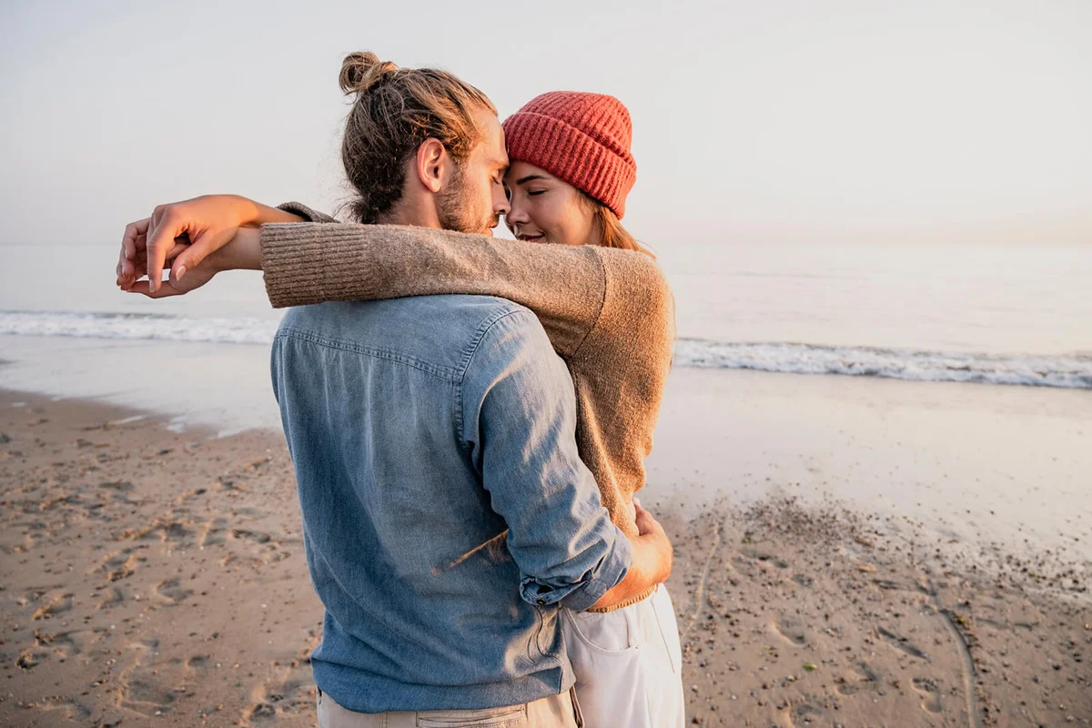 Young romantic couple standing face to face at beach against clear sky during sunset