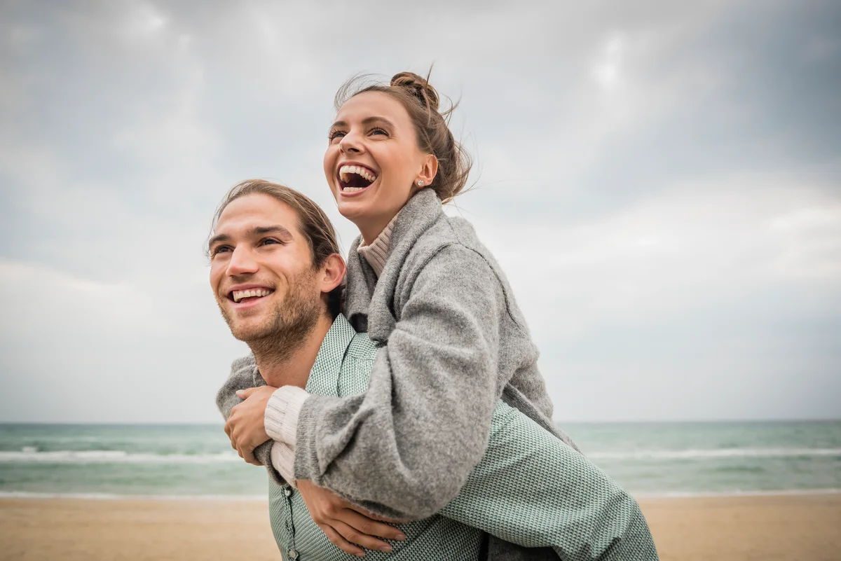 man carrying woman piggyback on beach