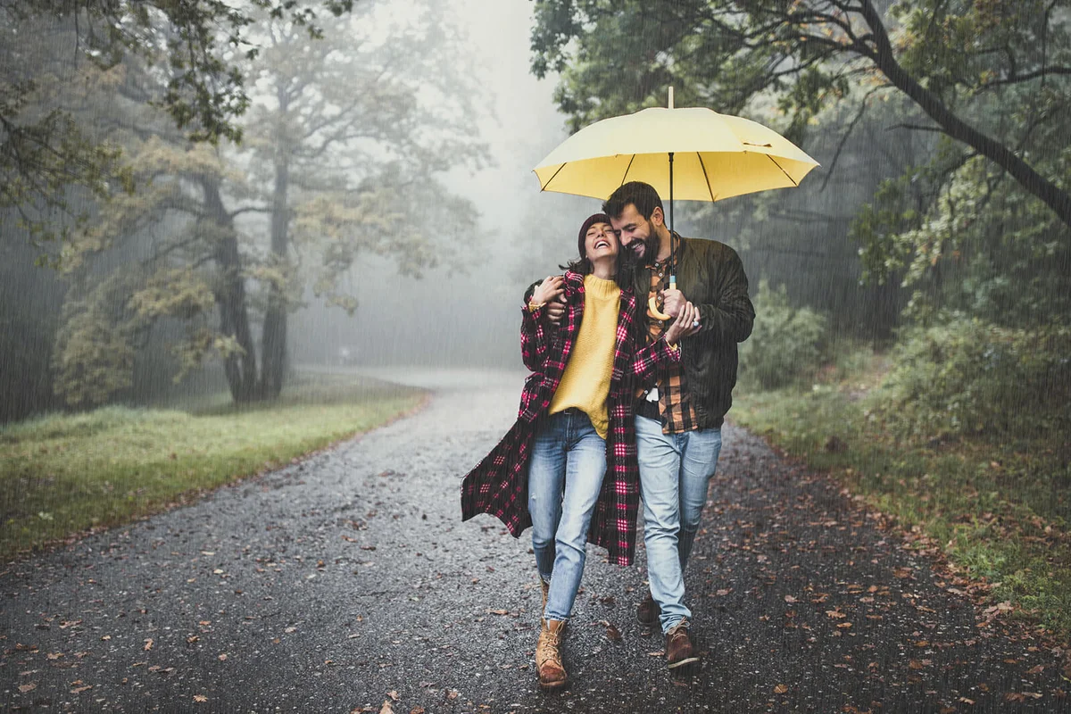 Happy embraced couple walking with umbrella at foggy forest