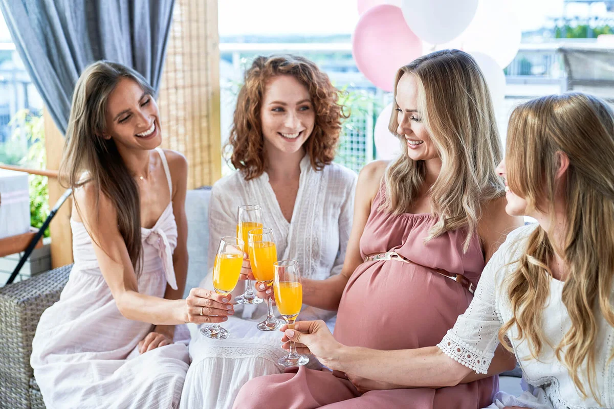 Smiling pregnant woman toasting cocktail glasses with friends