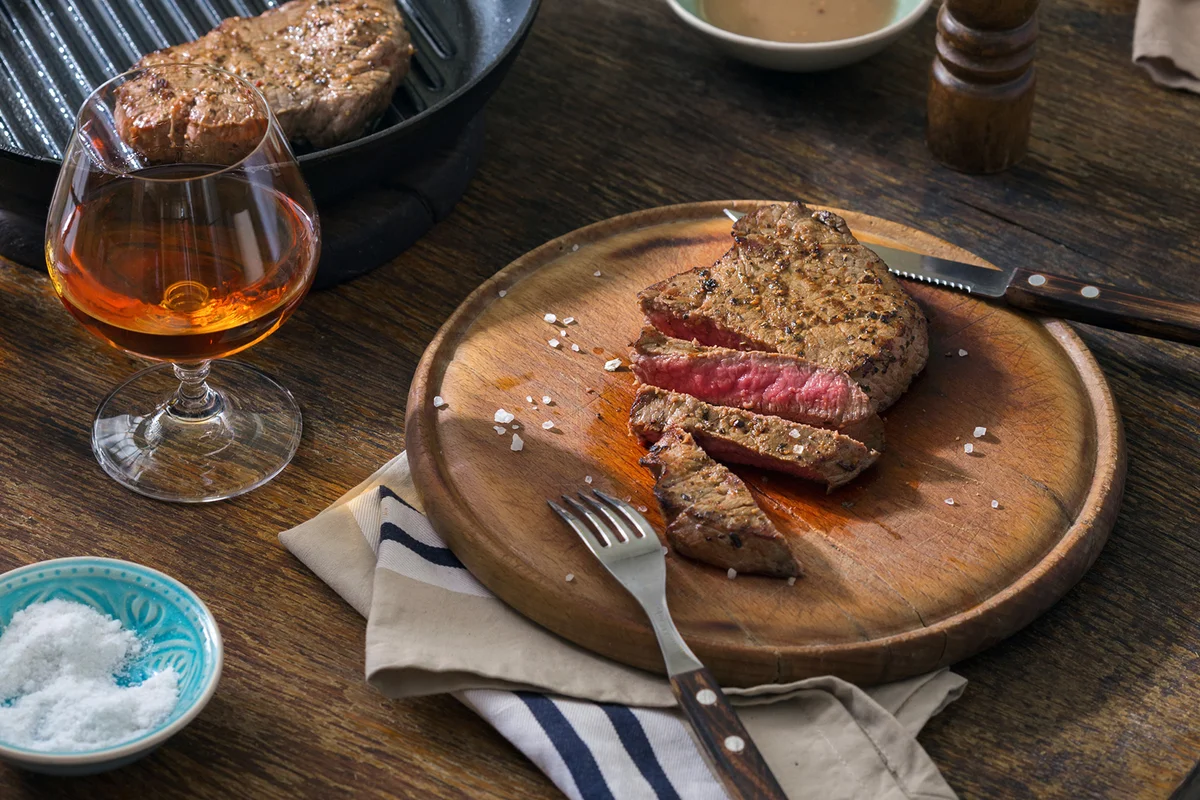 Beef rare grilled steak on wooden board with glass of whiskey