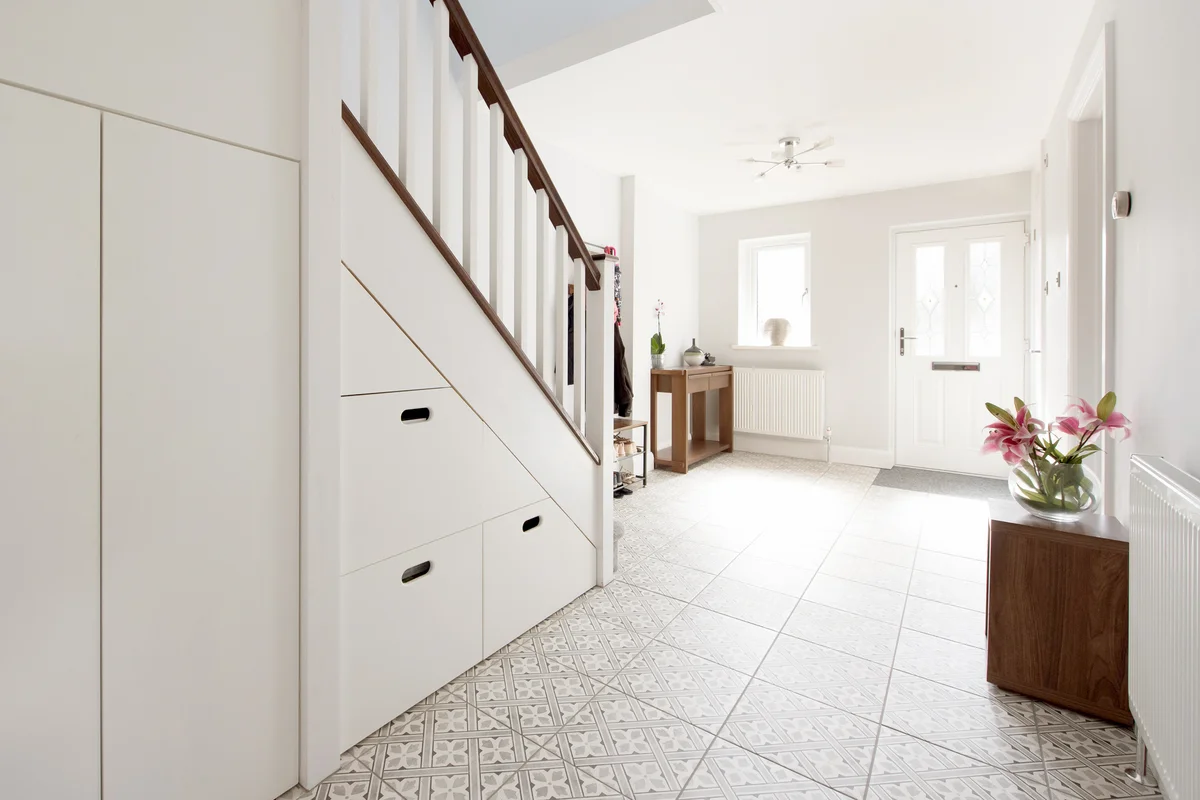Hall with patterned tiled floor and built in under stairs storage within a home