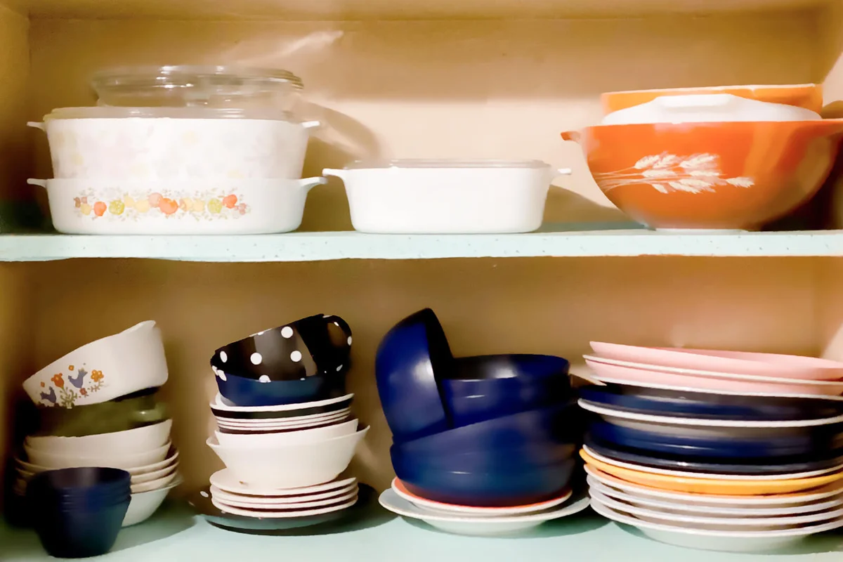 Vintage 1950s white wall kitchen cabinets open revealing shelves of old-fashioned kitchenware