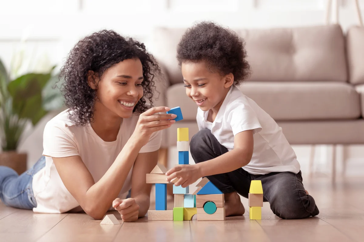 Babysitter with little kid son play with wooden blocks
