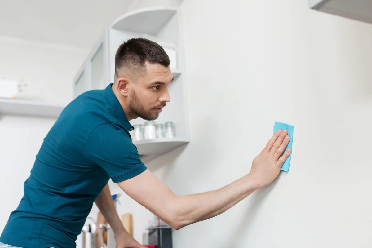 Man with rag cleaning wall at home kitchen