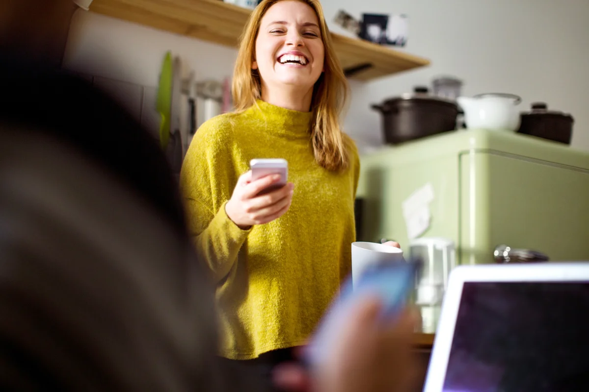 Cheerful woman with mobile phone in kitchen