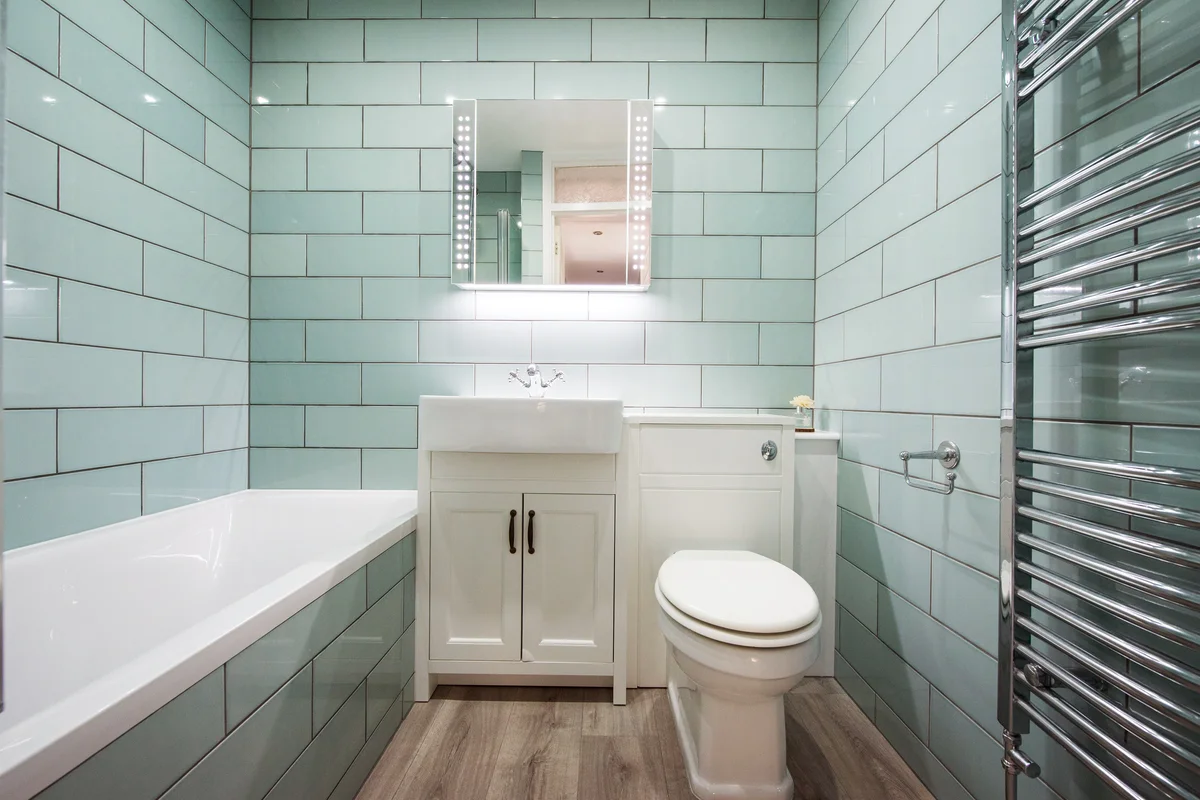 Small bathroom with green rectangular wall tiles, vanity mirror and cabinet