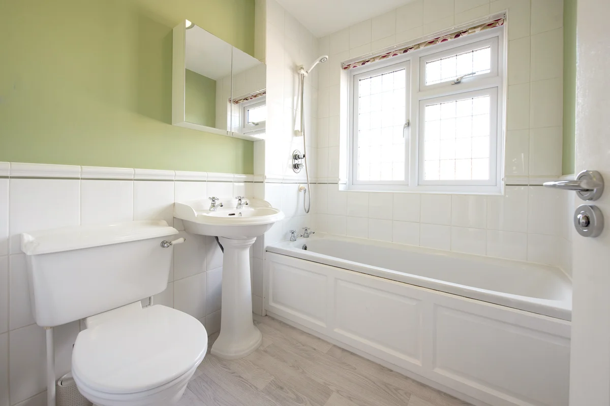 Small white tiled and green painted bathroom with mirrored cabinet