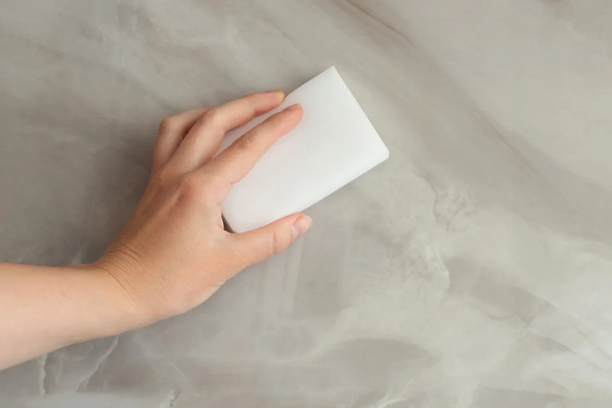A woman wipes a gray tile with a melanin sponge