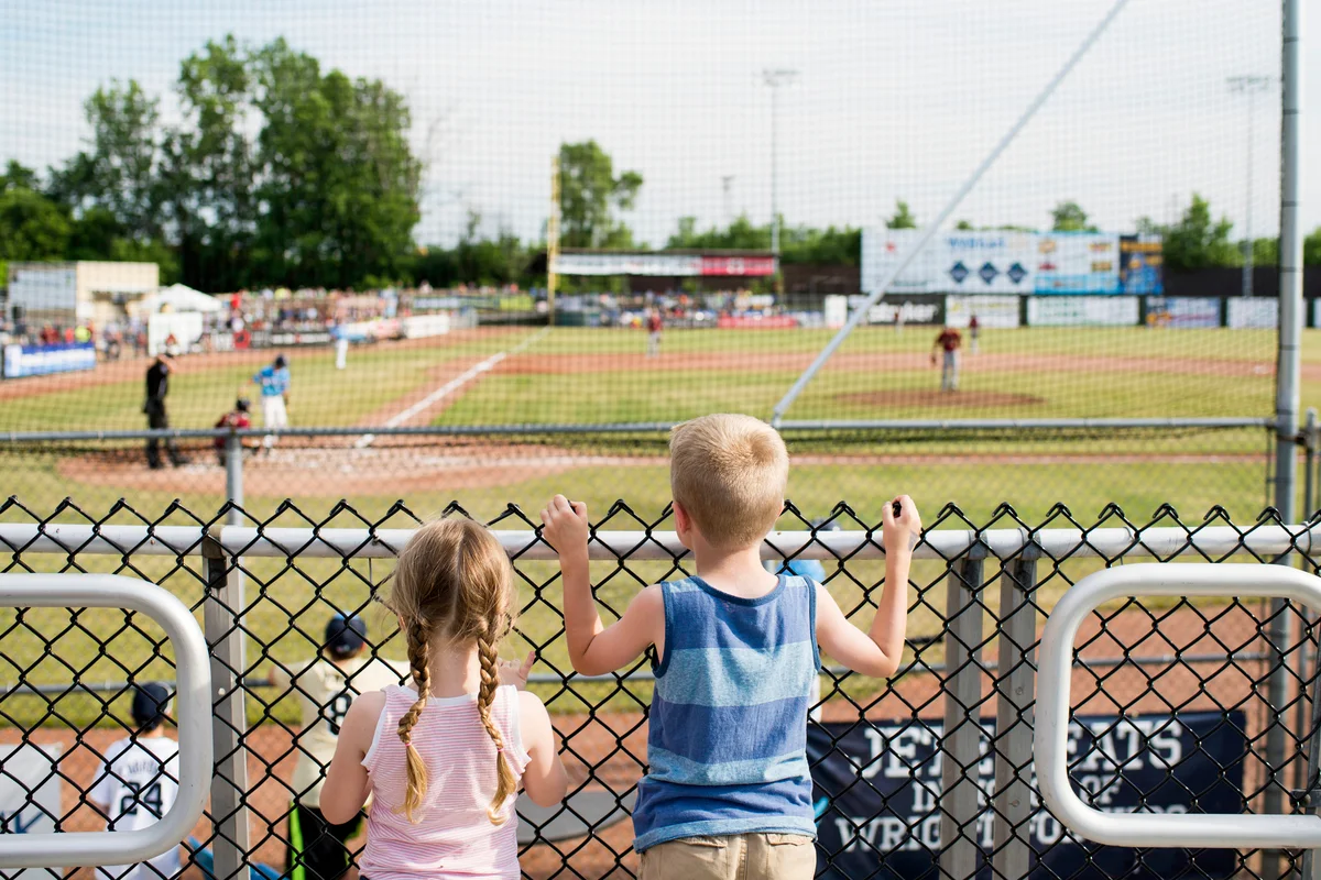 Siblings watching baseball match through fence at stadium
