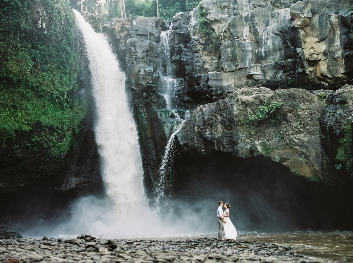 Young beautiful couple in wedding clothes exploring amazing waterfall.