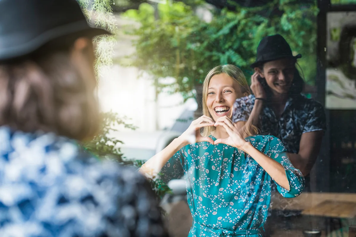 Beautiful young woman making a finger frame heart and smiling at her boyfriend through a window