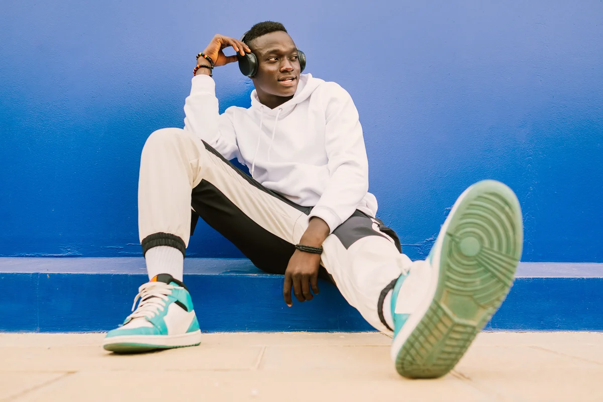 Man in track suit and vintage sneakers sitting against blue wall