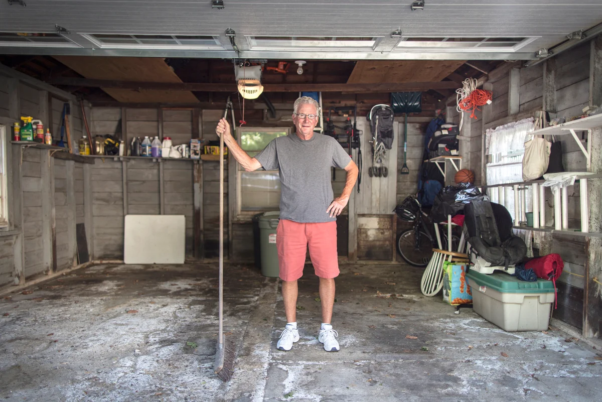 Man standing in front of the garage holding broom