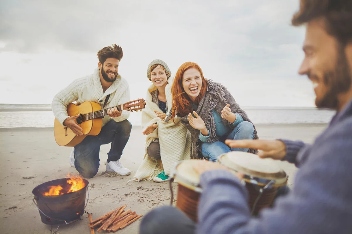 Friends making music around camp fire on beach