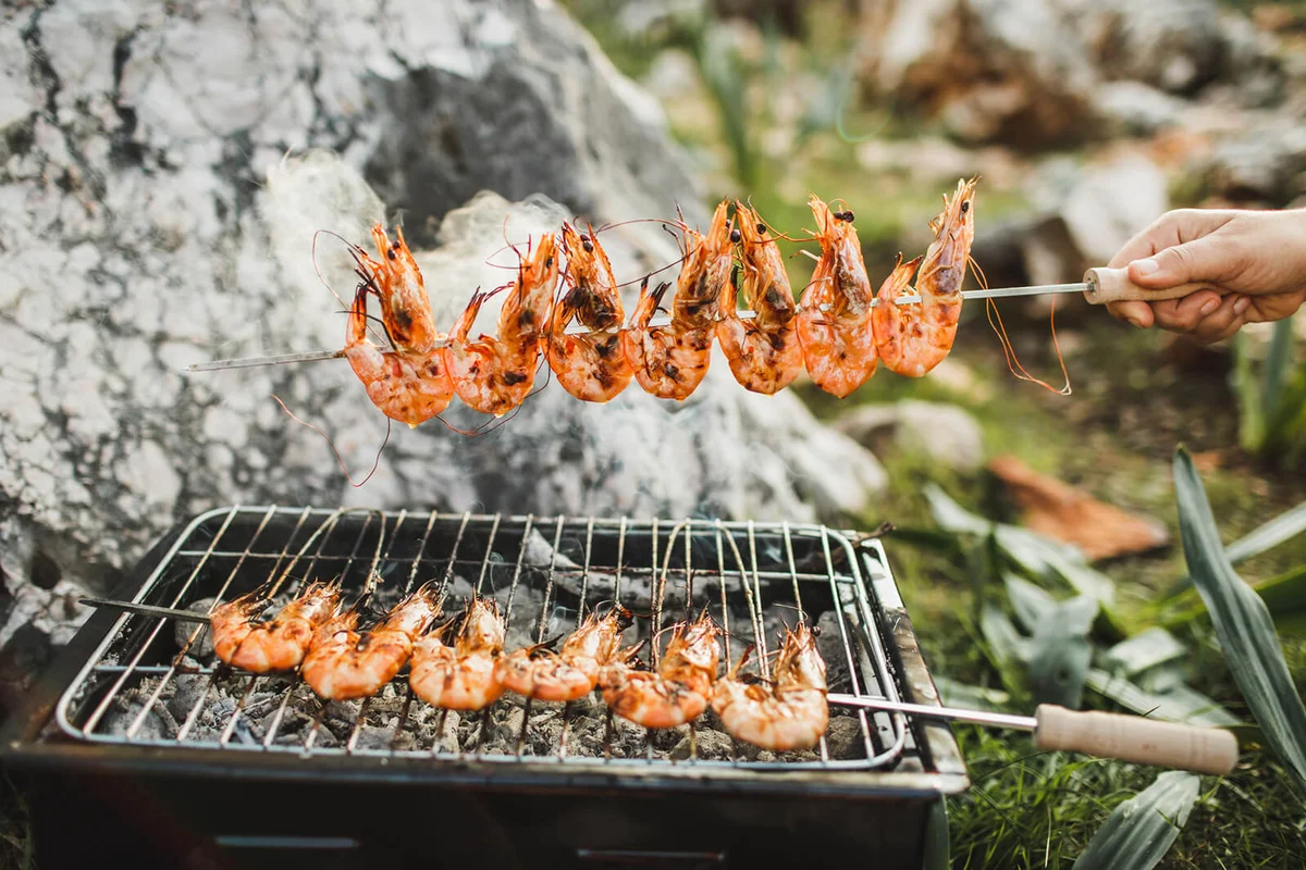 man's hands cooking grilled shrimps on barbecue