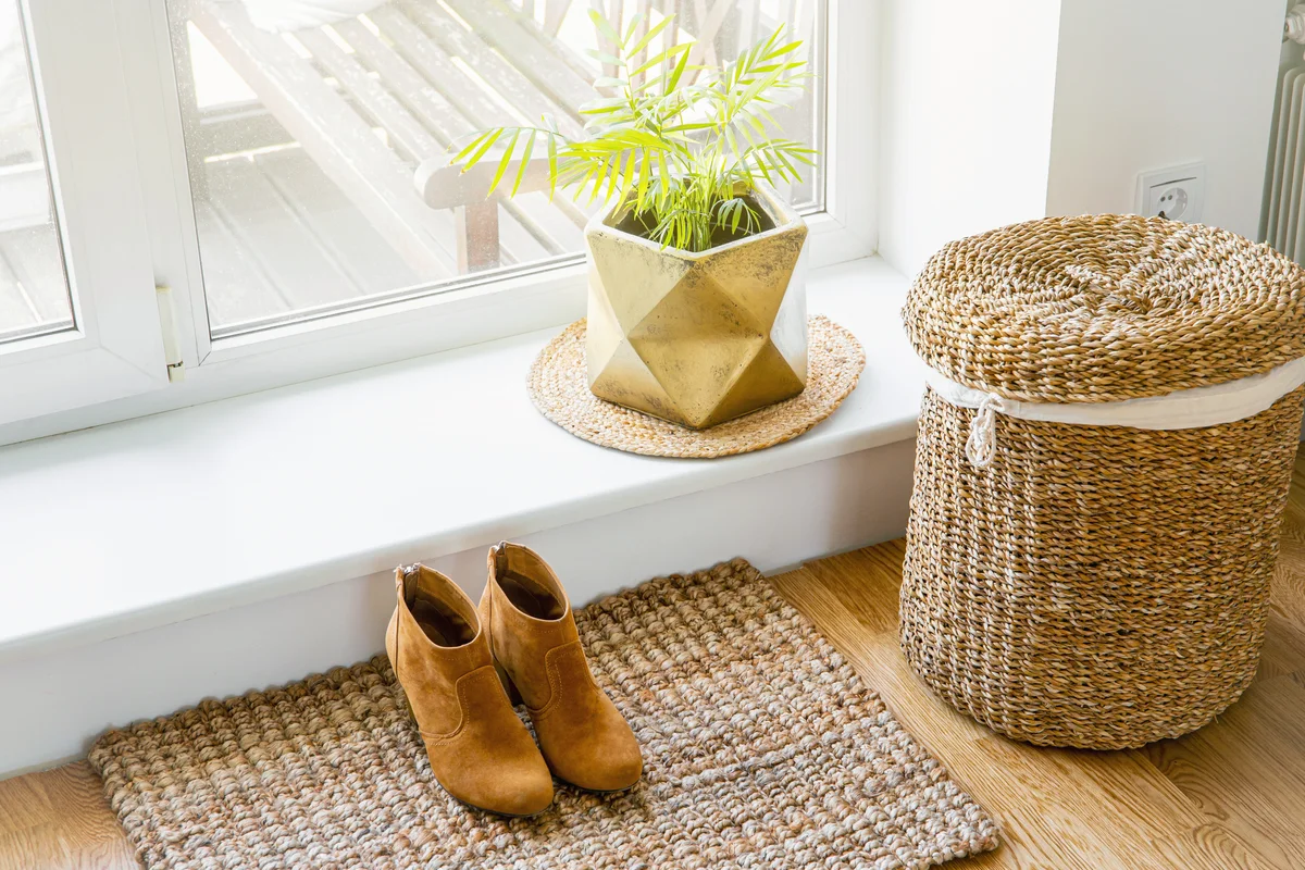 Hardwood floor with jute doormat, flower pot and laundry basket by window