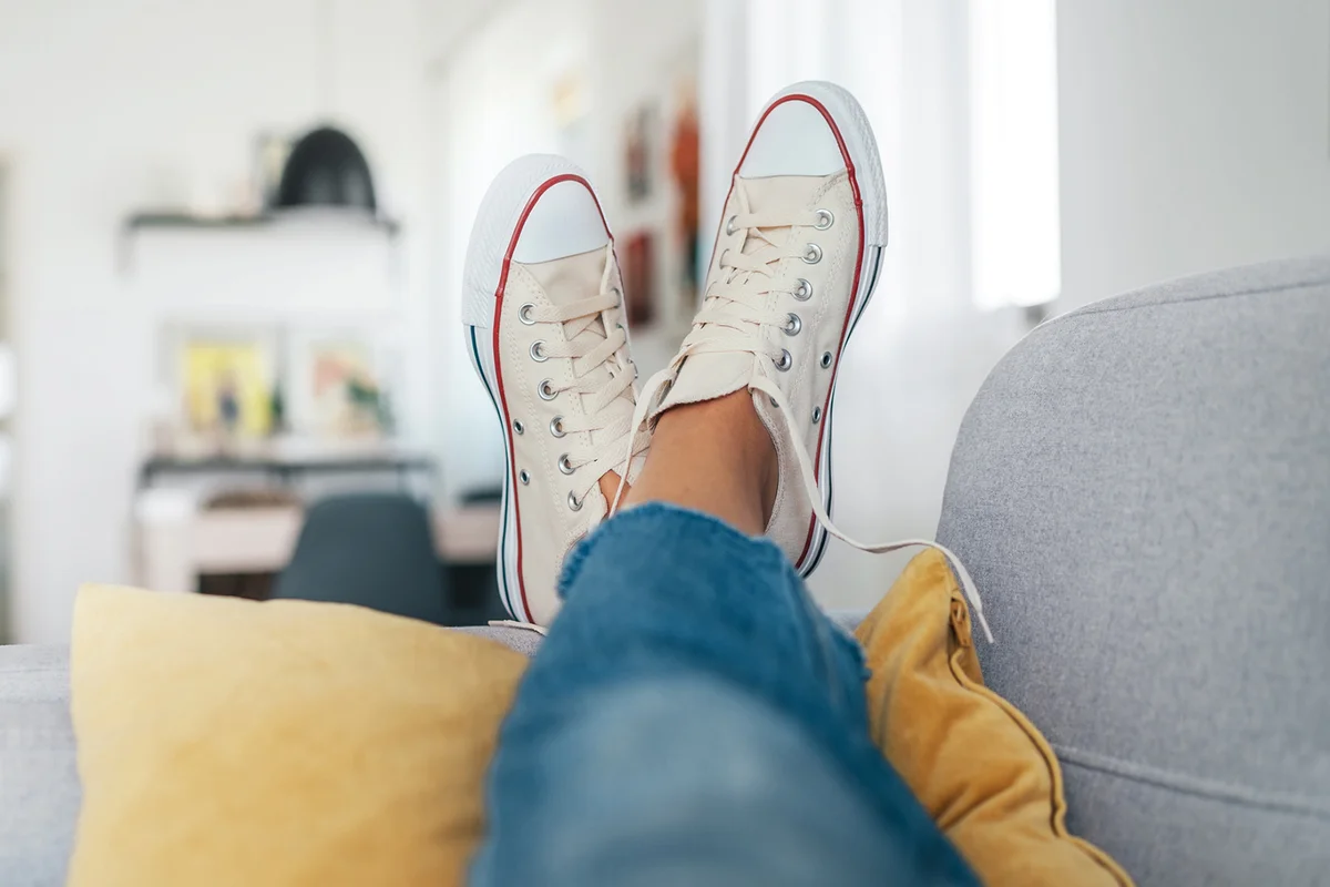 Young female lying in new beige sneaker son cozy comfortable living room sofa putting feet on pillows and resting and relaxing