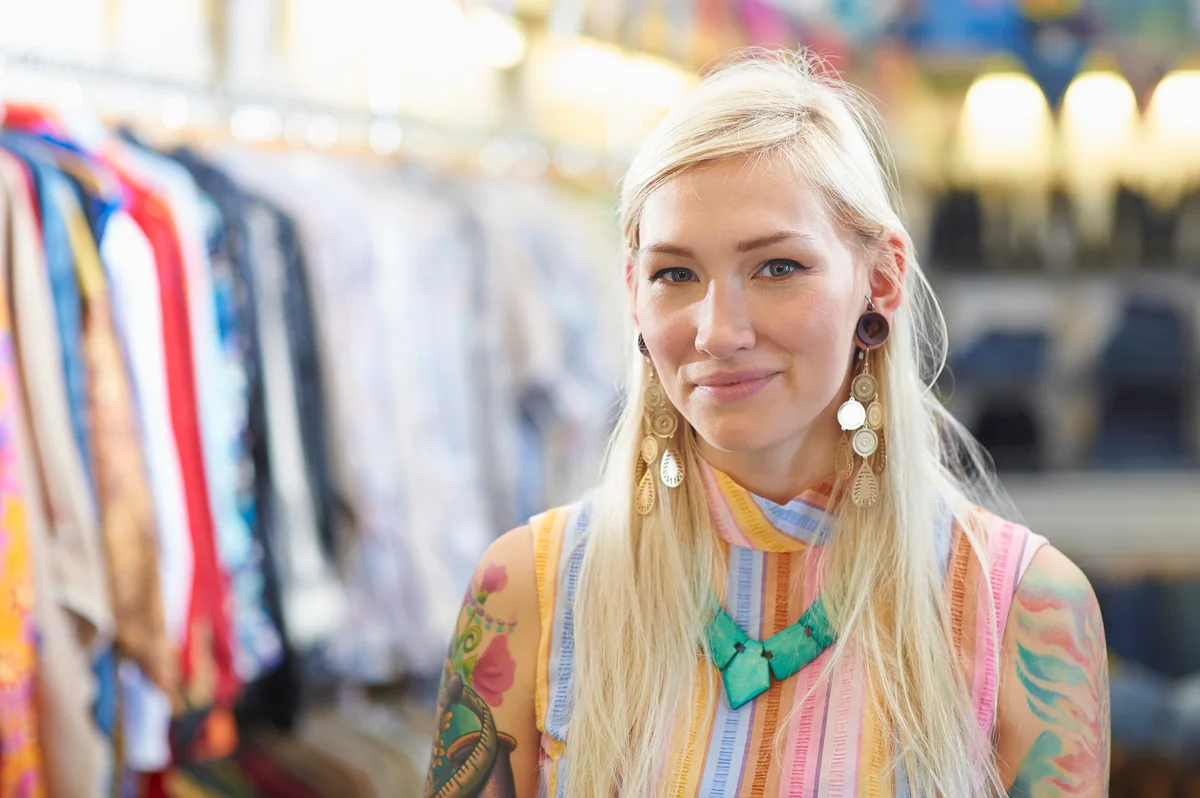woman wearing colorful shirt, cool earrings, and blue-ish green bib necklace.