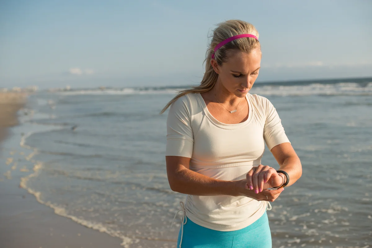 athletic woman on beach checking her fitness watch wearing light-weight necklace