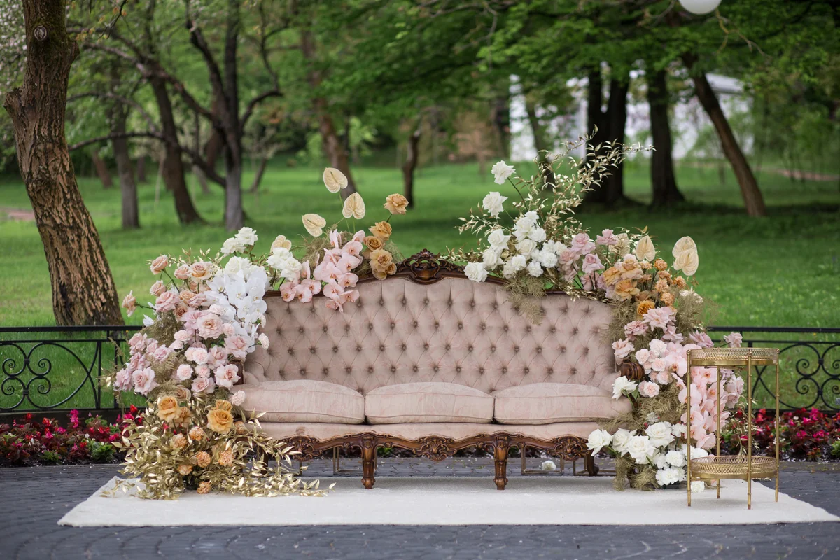 View of pink sofa decorated with flowers during wedding reception with park on the background.