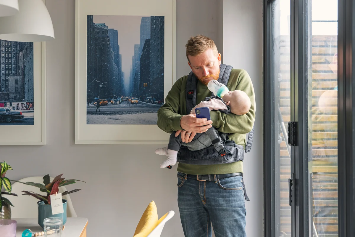 dad looking at phone while holding baby