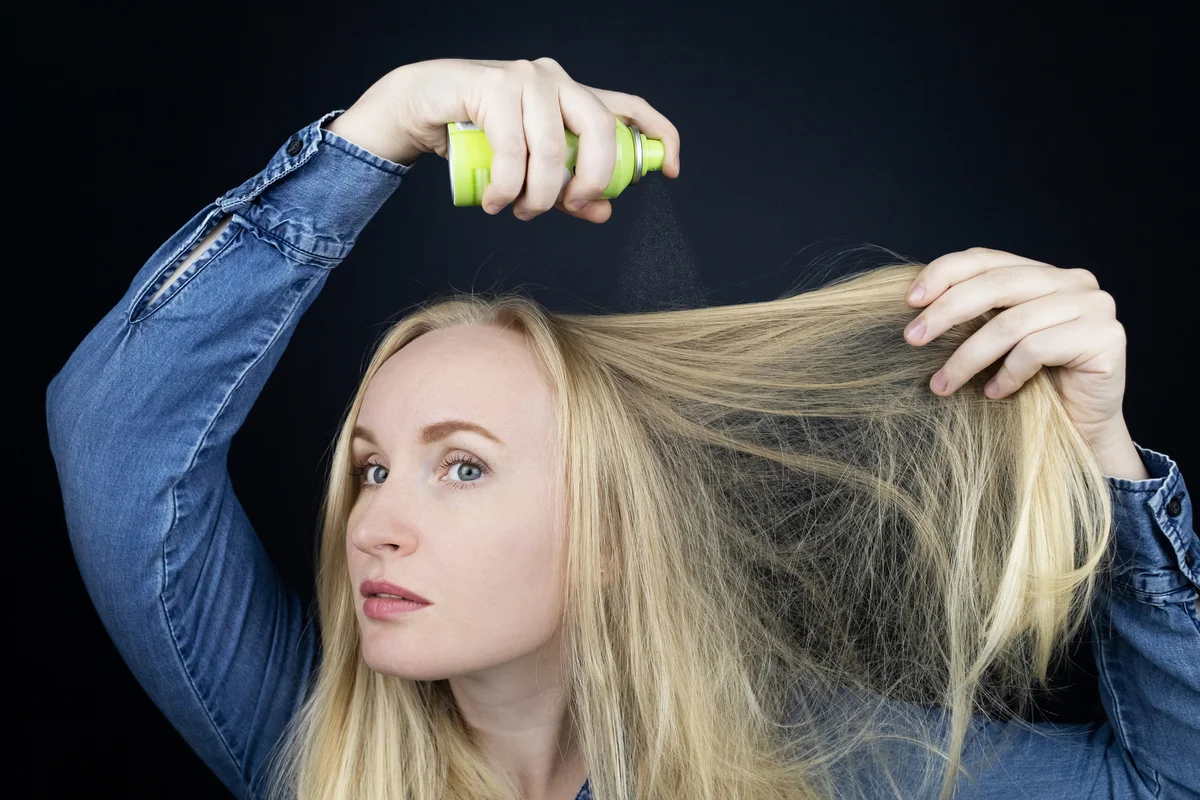 woman spray hair with dry shampoo