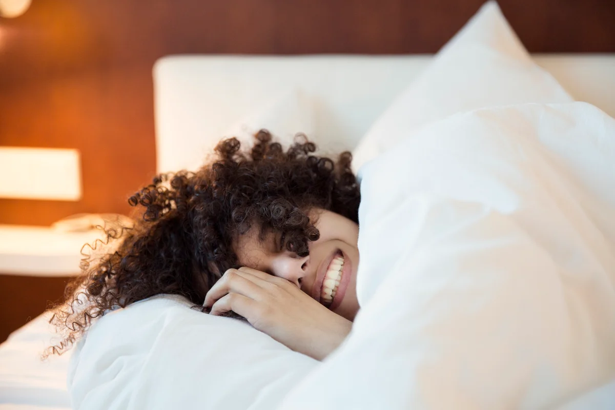 smiling woman with curly hair laying head on pillow