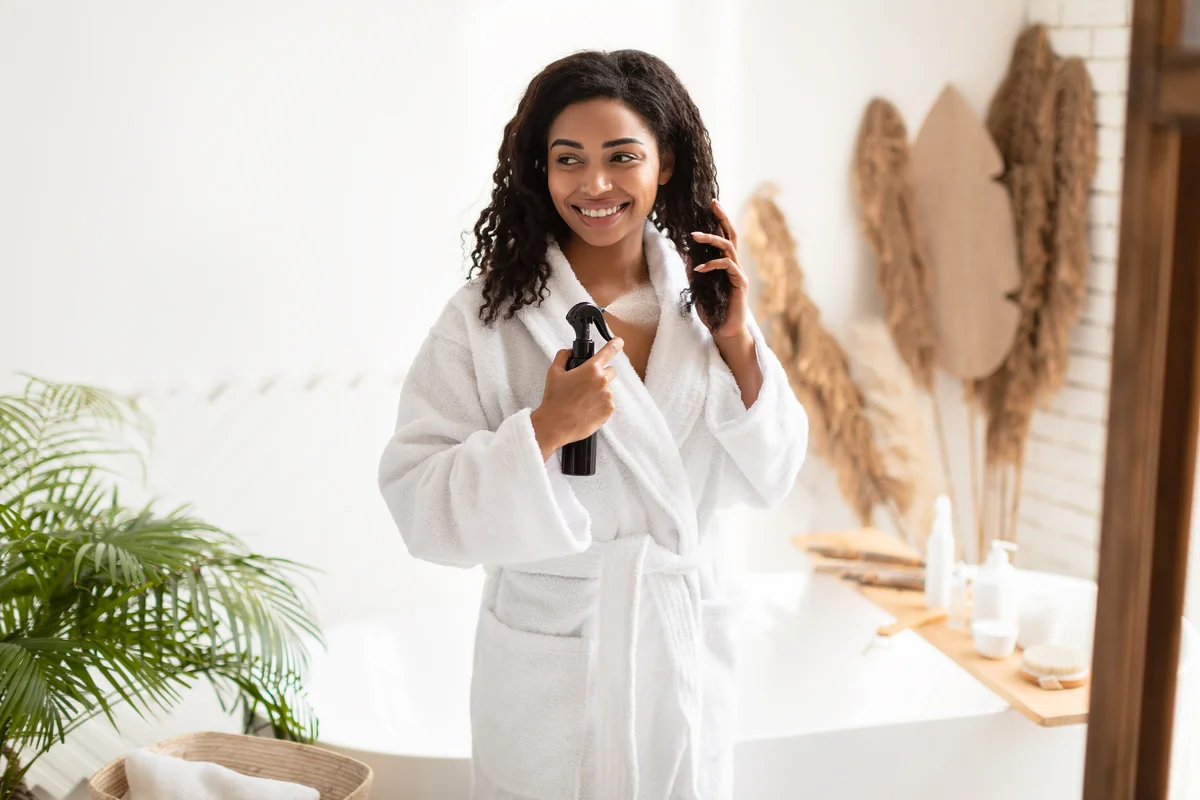 young woman in robe spraying her natural hair