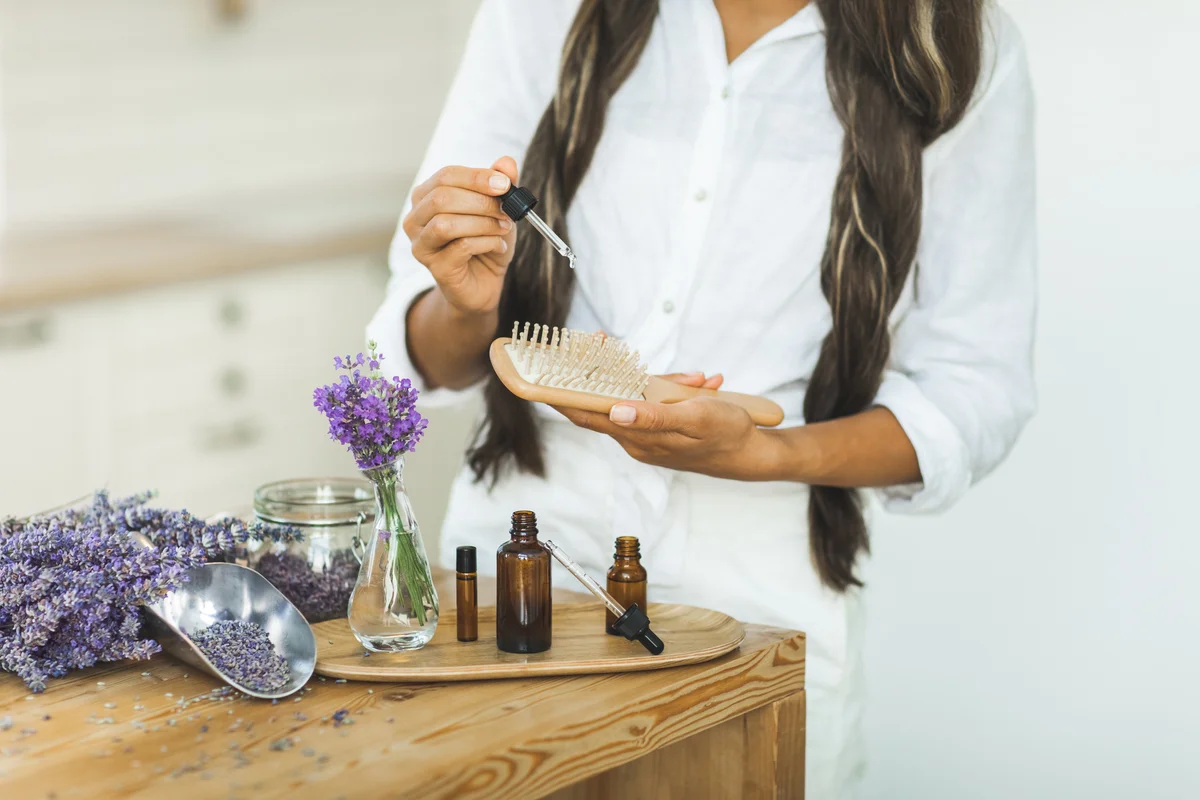 woman with long hair dropping scented oil onto a hairbrush