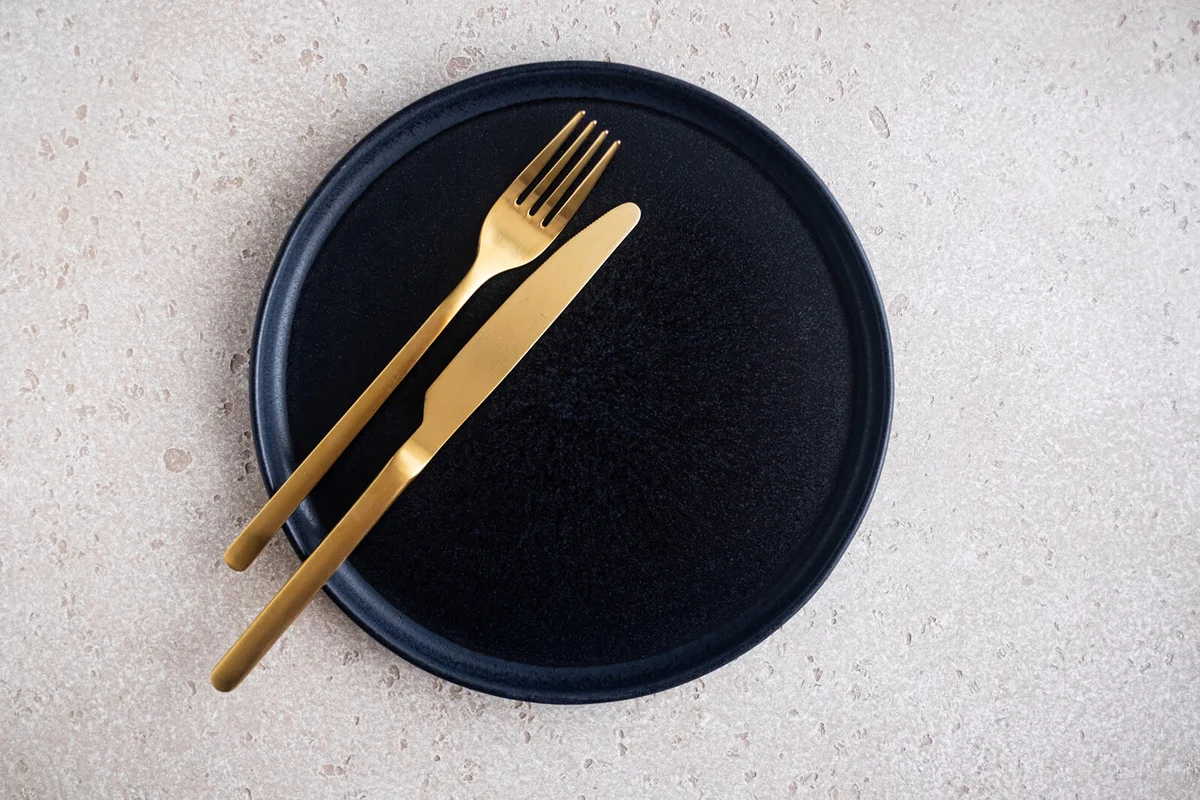 Empty black ceramic plate and golden fork and knife