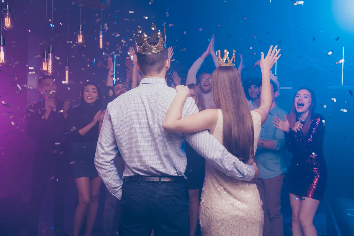 prom king and queen facing crowd of cheering friends