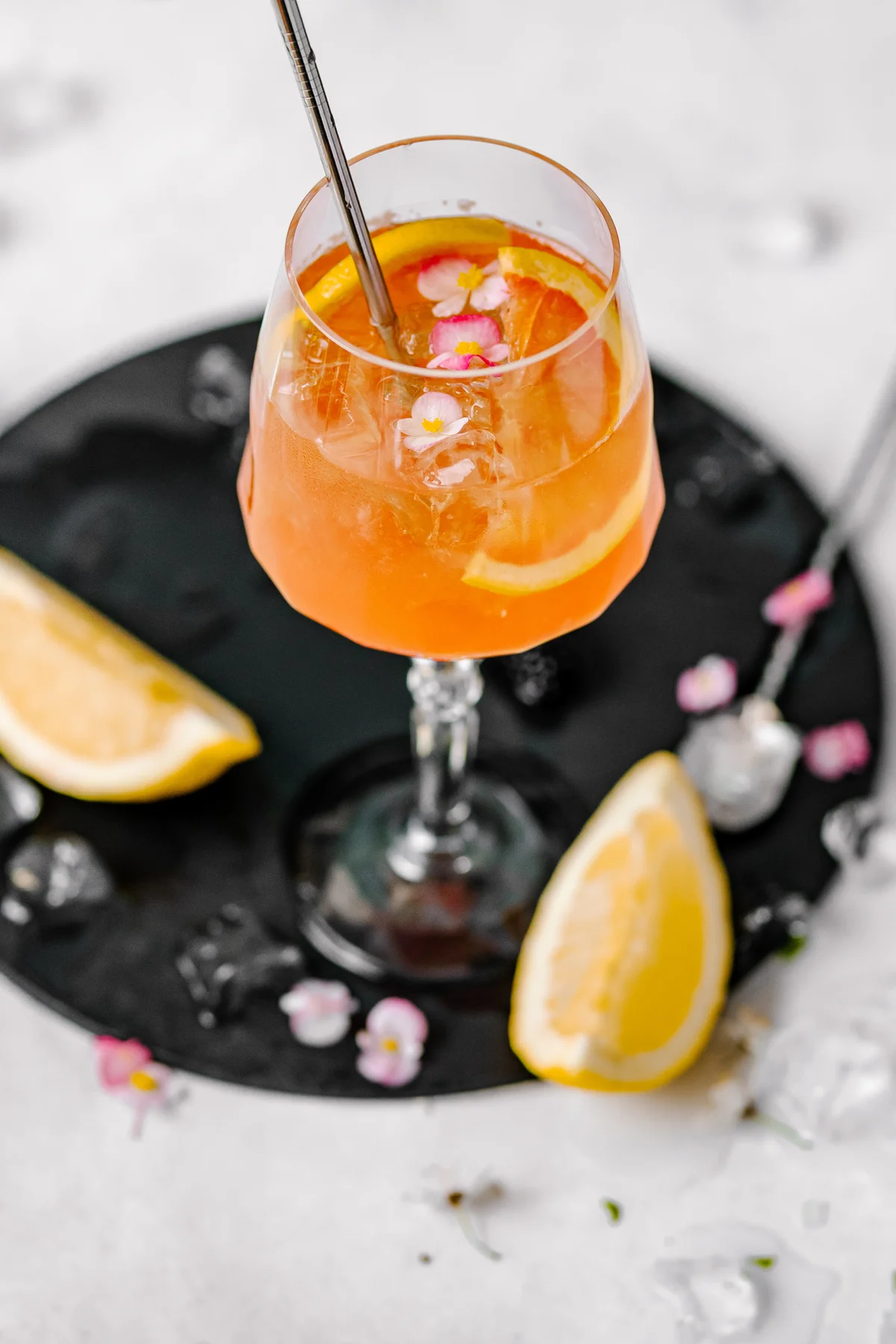 Iced orange drink in a wine glass garnished with flowers