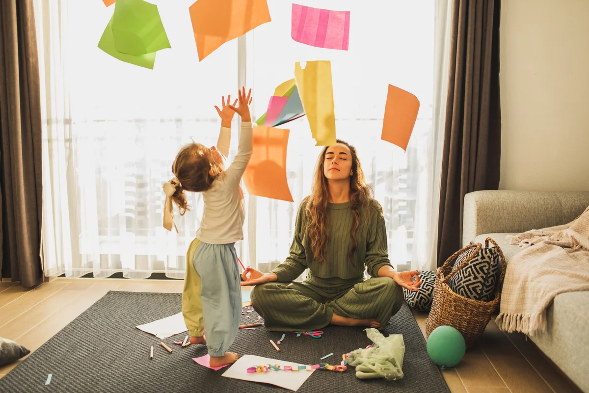 child throws papers while mom meditates in background