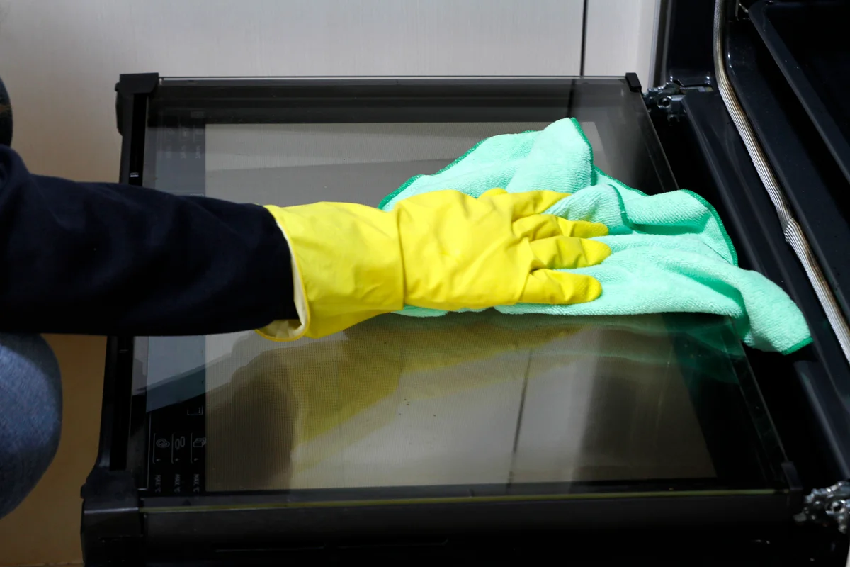 gloved hand wiping inside oven glass