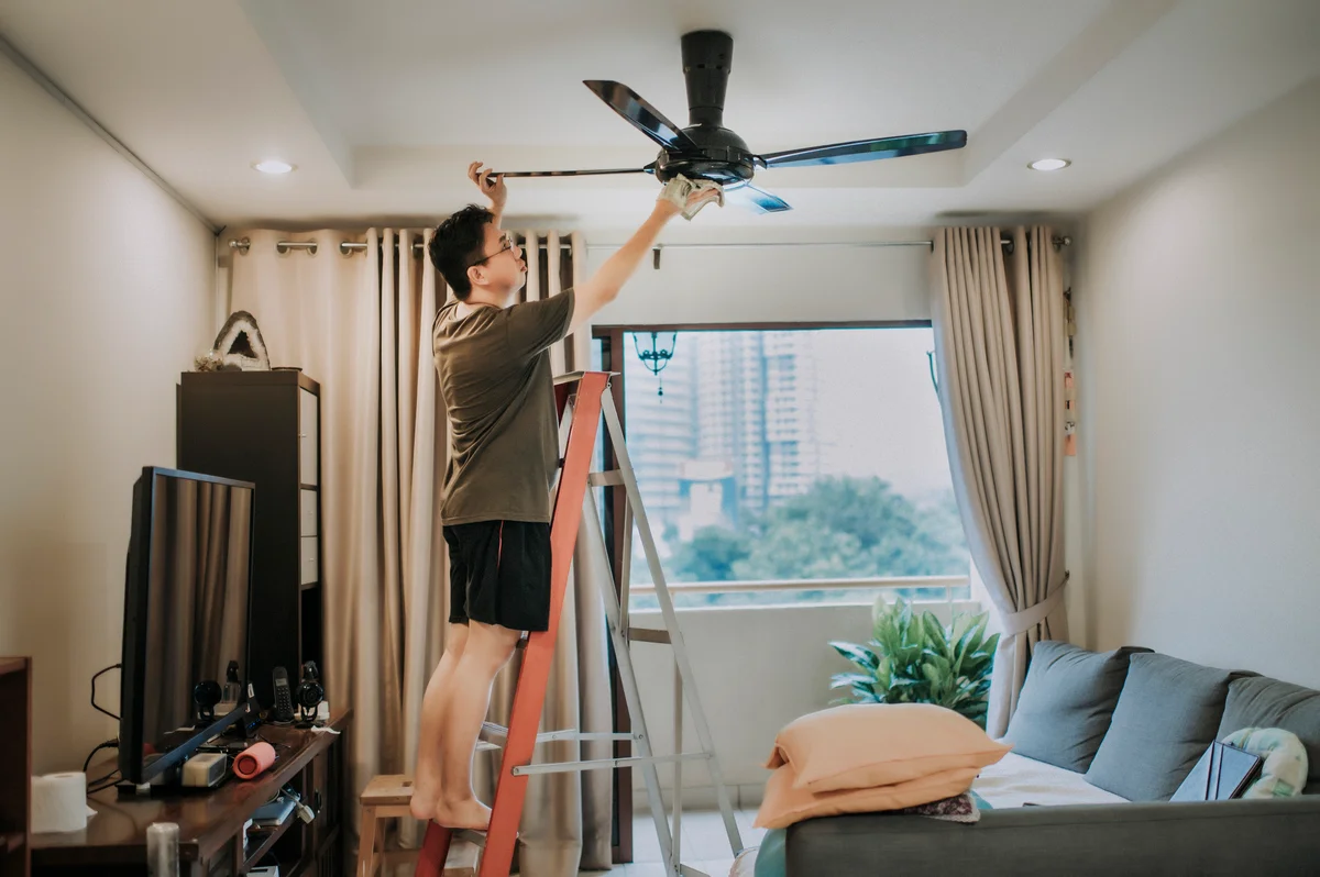 man on step ladder dusting ceiling fan