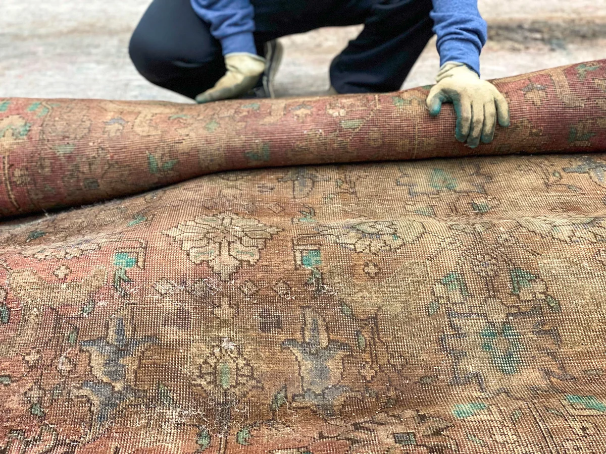 person wearing gloves rolling up dirty rug