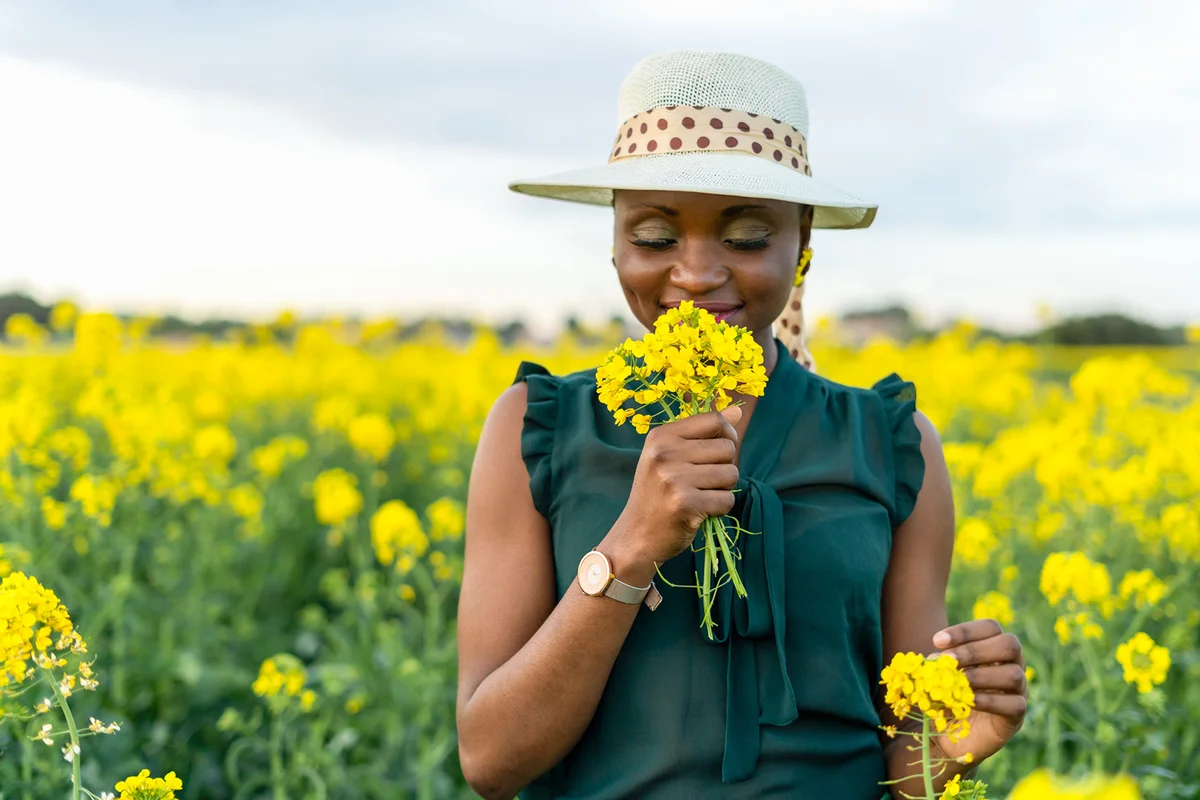 Woman portrait holding and smelling yellow flowers bouquet on colorful countryside field
