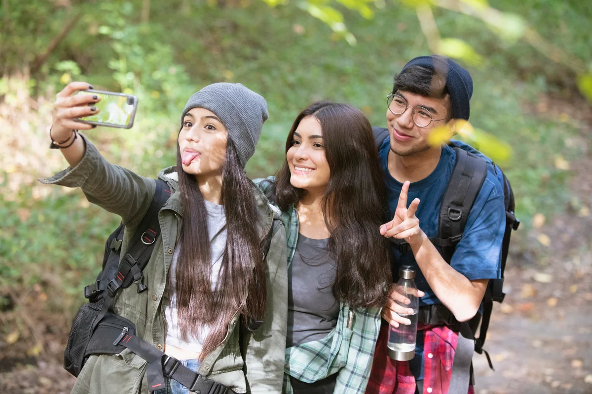 Two girls and a boy in woods hiking, stopping to take a selfie